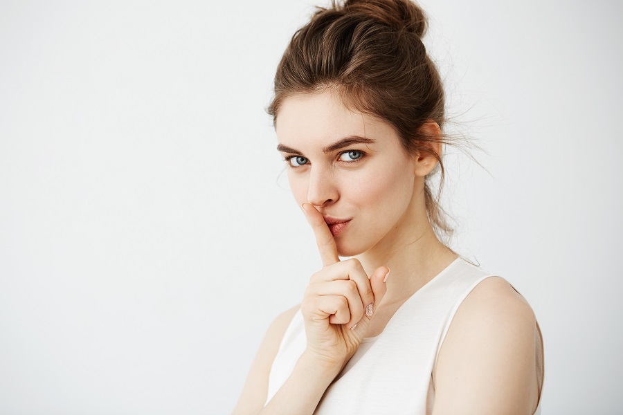 Portrait of young beautiful girl showing keep silence looking at camera over white background.